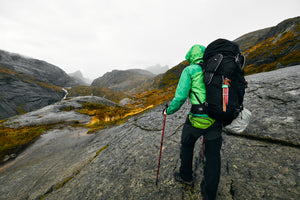 A rain-drenched hiker in full zip rain pants and a rain jacket makes his way through the mountains.