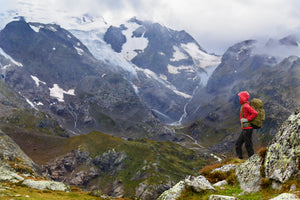 A hiker in a rain jacket overlooks a mountain vista.