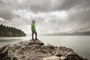 A hiker in full rain gear looks out over a lake in rainy conditions.