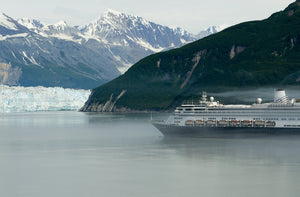 An Alaska cruise ship passes by a glacier backed by snow-capped mountains.